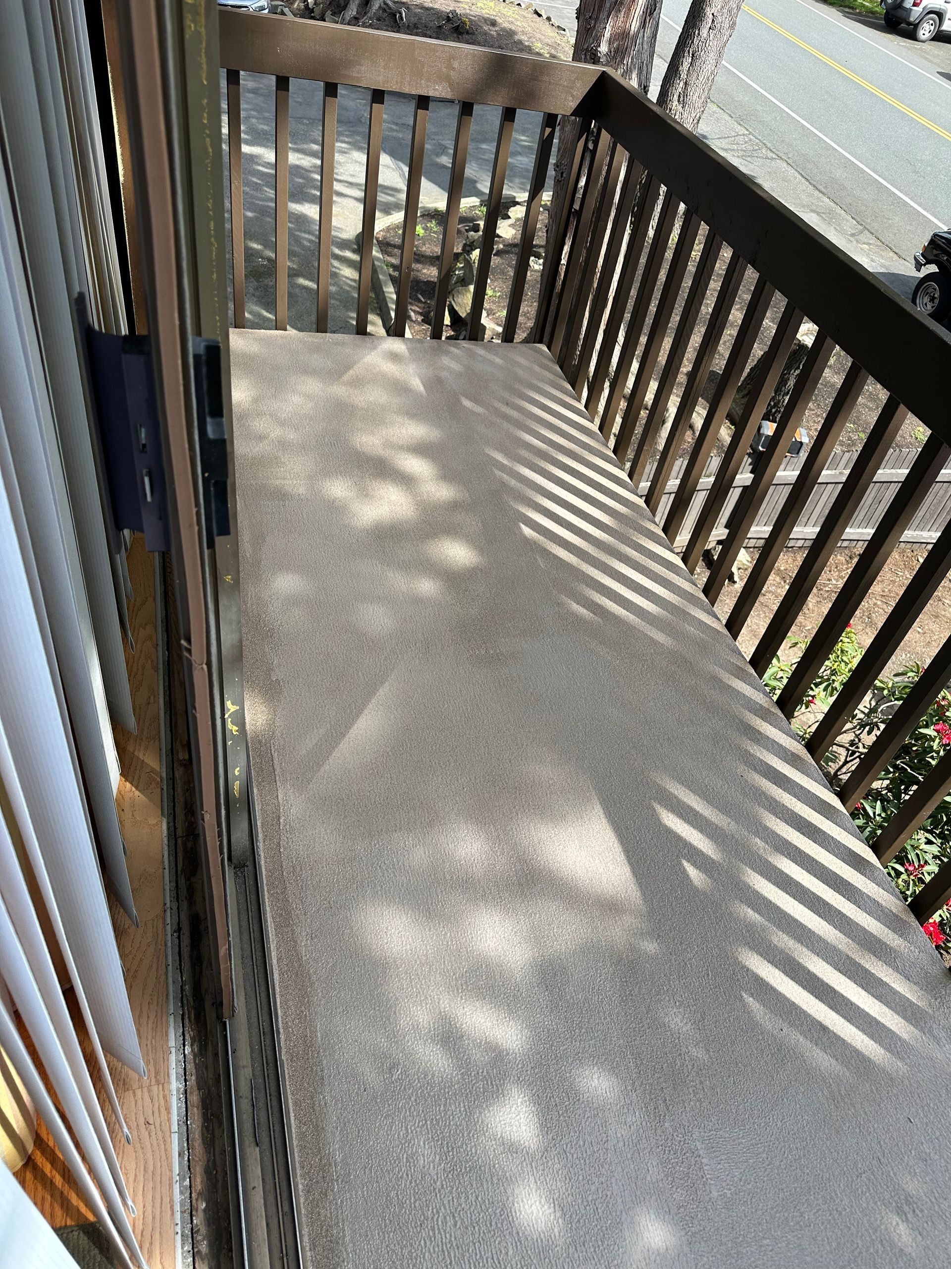 Small wooden balcony with concrete floor and railing, beside a road in daylight.