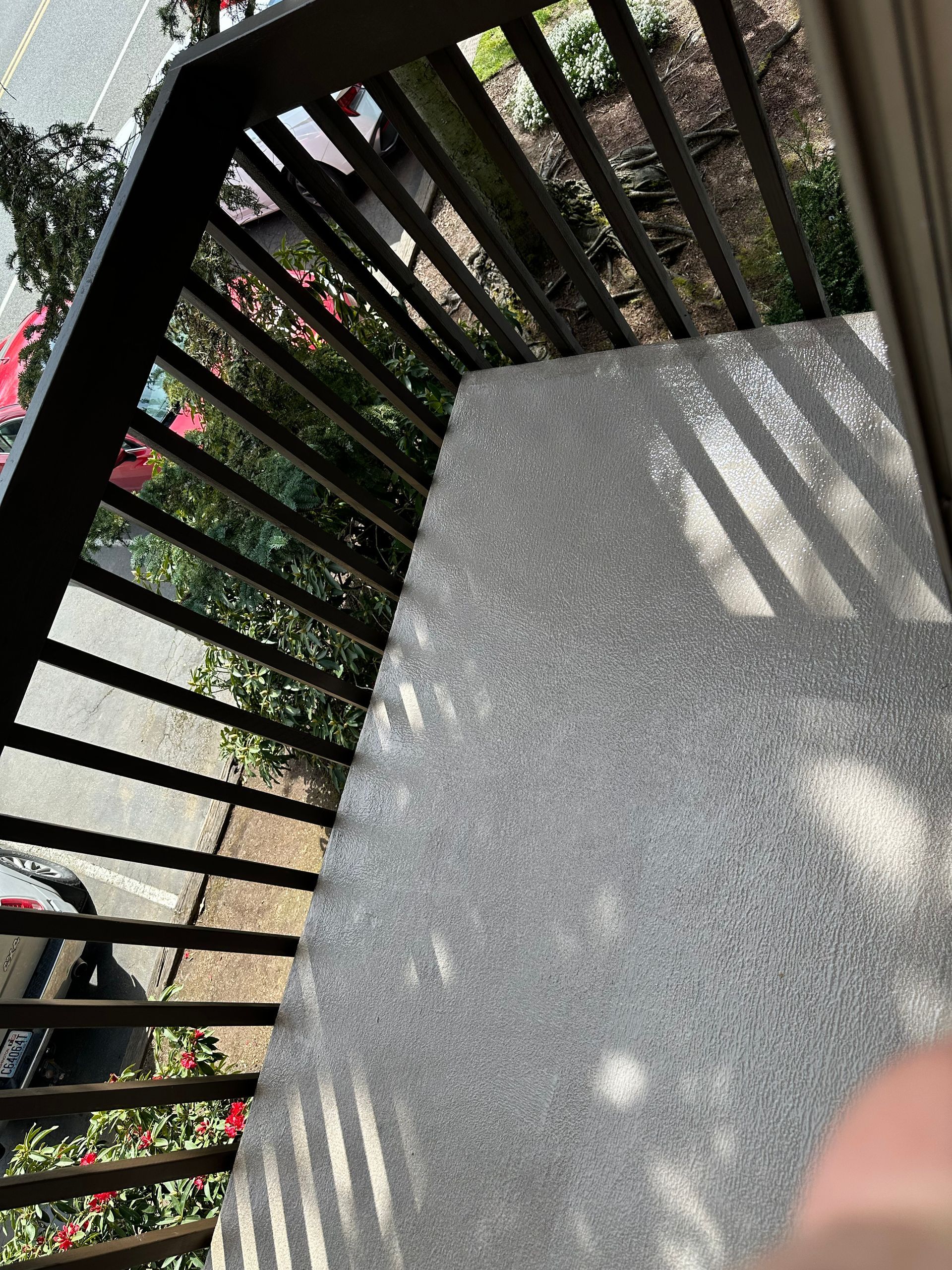 Concrete balcony floor with black railing casting diagonal shadows over potted greenery below