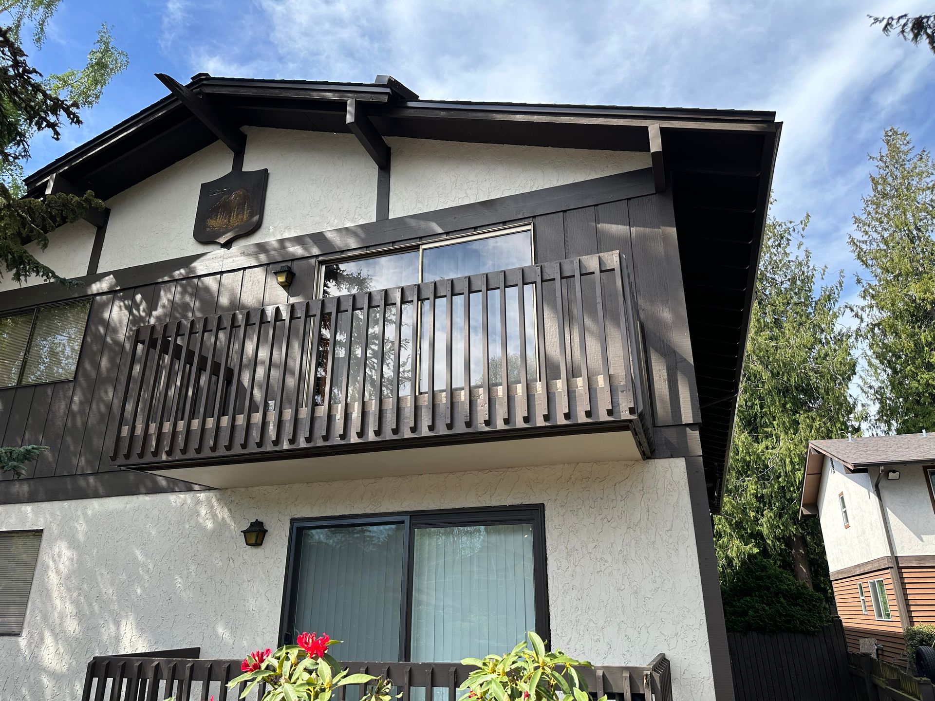 Two-story white house with a wooden balcony, sliding glass door, and red flowers under a blue sky