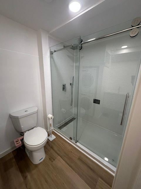 Small bathroom with a toilet, wood floor, and a glass-enclosed shower.