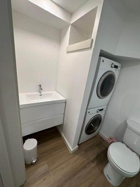 Compact bathroom with sink, stacked washer-dryer, and toilet on wood flooring