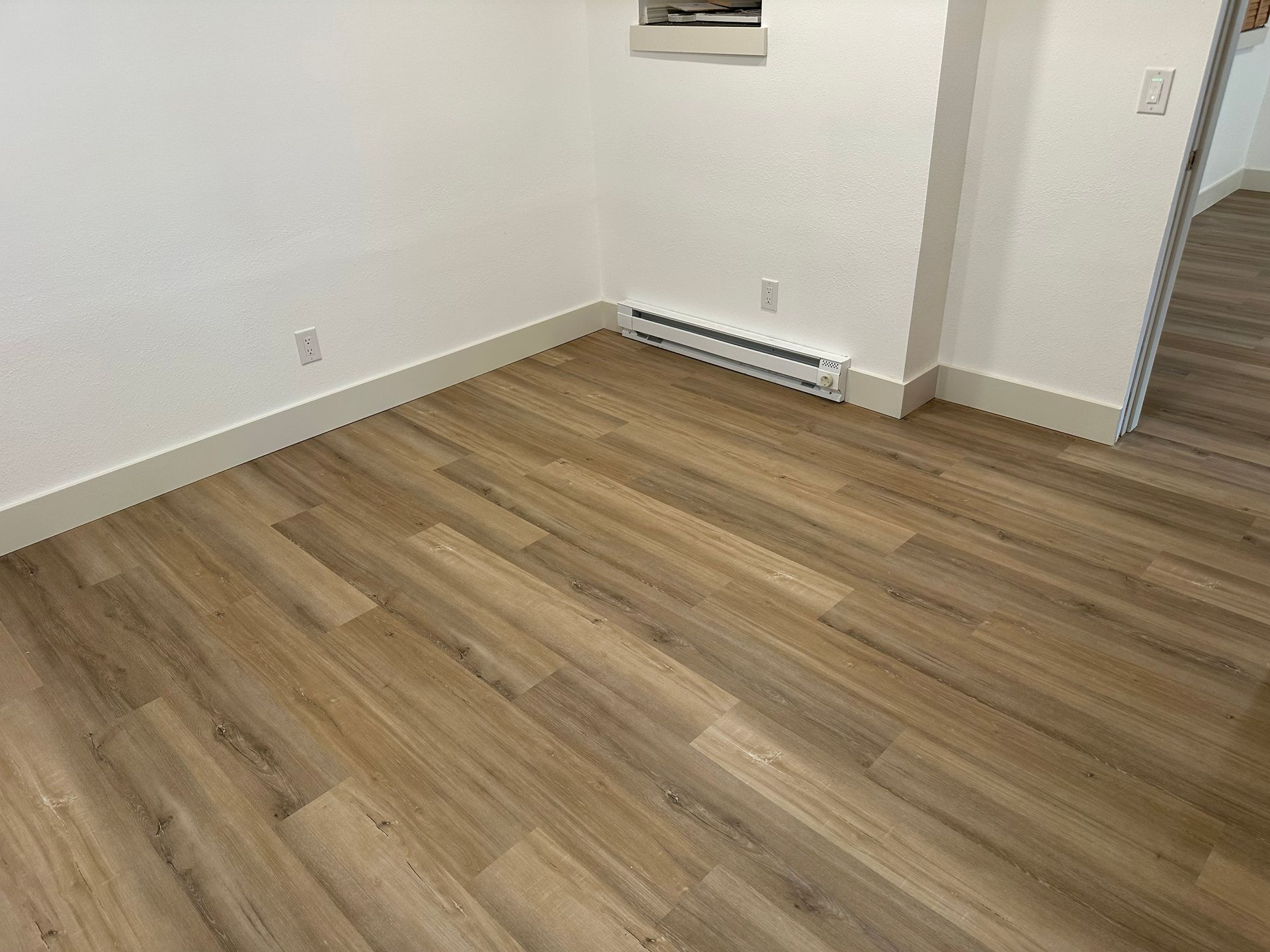 Empty room with wood flooring, white walls, and a wall-mounted heater near a doorway.