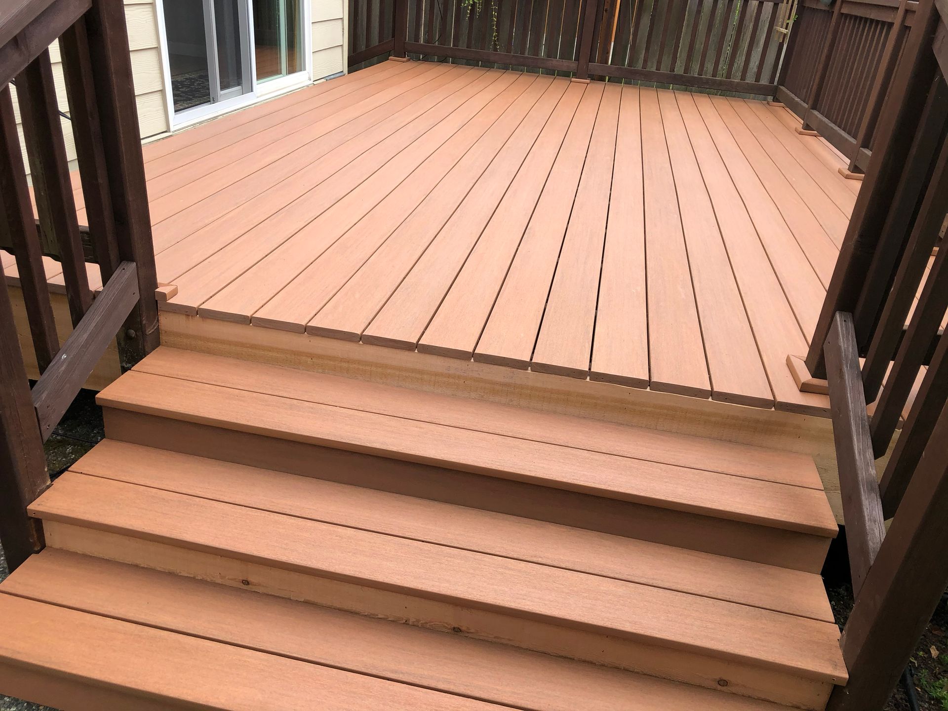 Wooden deck with three steps leading to a brown fenced patio.