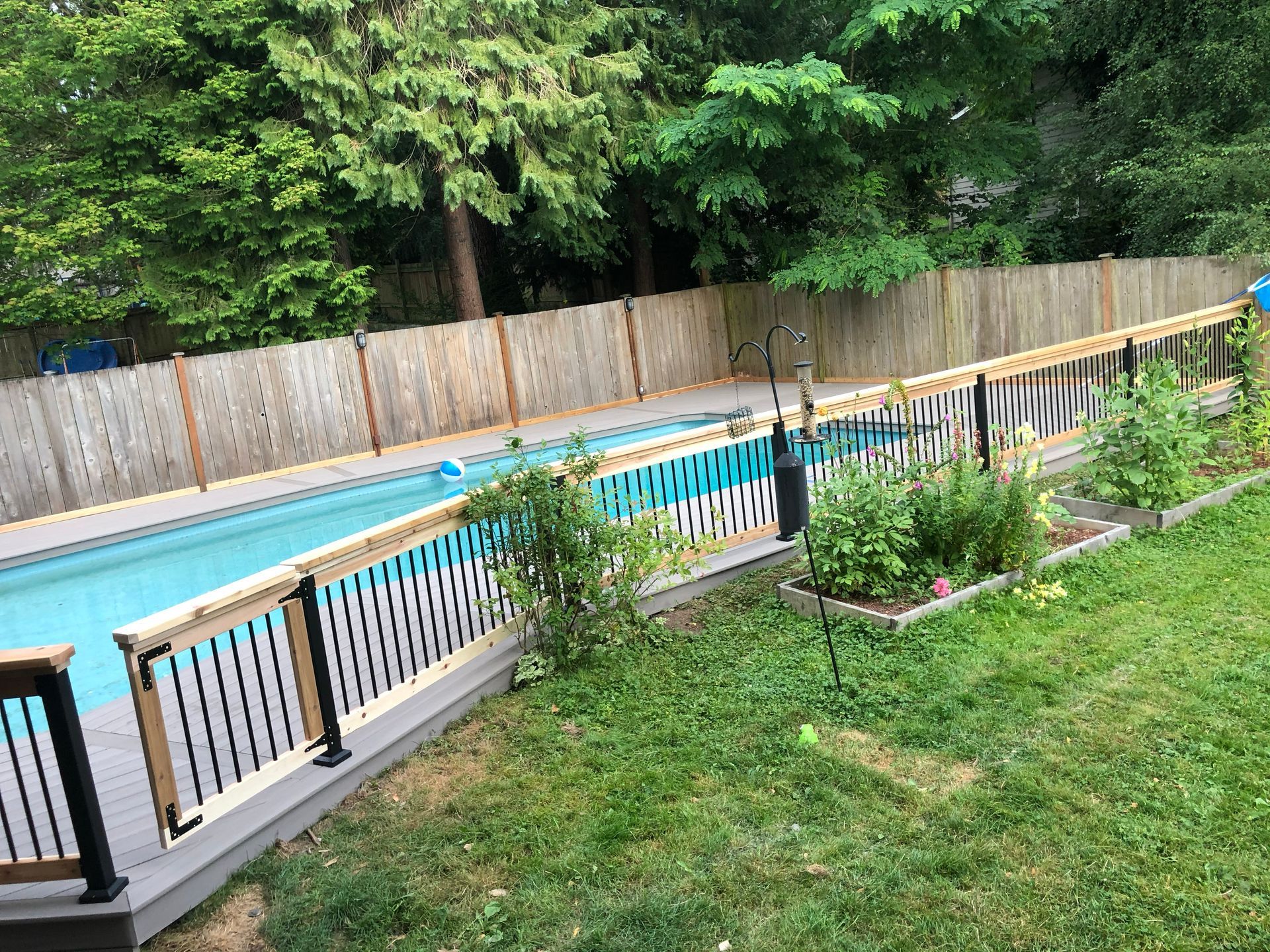 Outdoor swimming pool with a black fence, patio chairs, and a grassy yard beside a wooden privacy fence