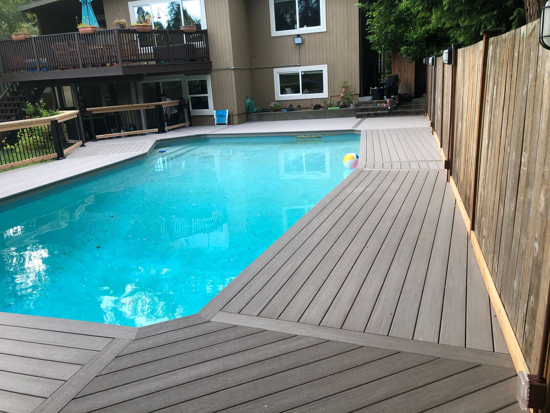 Backyard swimming pool with gray deck and fence, turquoise water, and a small float near the edge