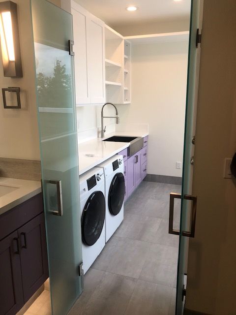 Small laundry room with white countertop, sink, open shelves, purple cabinets, and a washer and dryer.