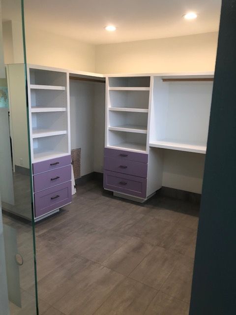 Empty walk-in closet with white shelving, purple drawers, and gray flooring under ceiling lights