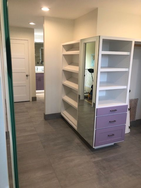 Walk-in closet with white shelving and purple drawers in a hallway with gray flooring
