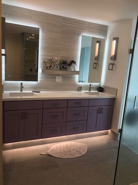 Modern bathroom vanity with purple cabinets, double sinks, mirrors, and soft under-cabinet lighting.