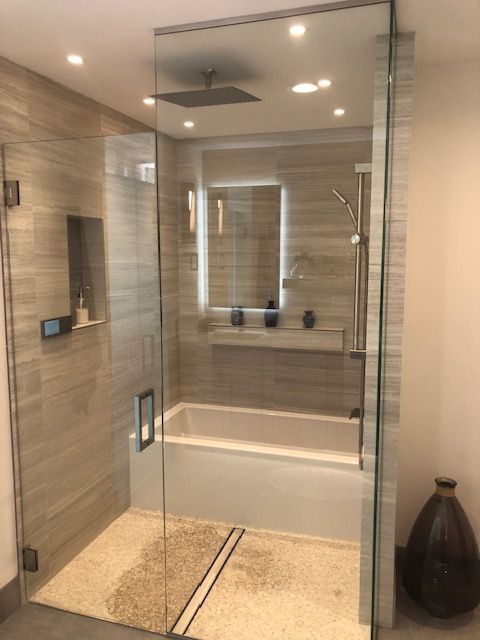 Modern glass walk-in shower with beige tile, built-in bench, and rainfall showerhead.