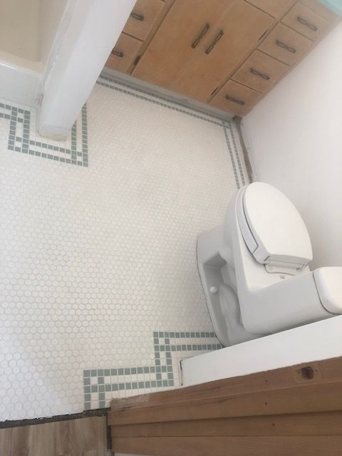 Small bathroom with white mosaic floor, wood cabinets, and a toilet beside a shower curtain.