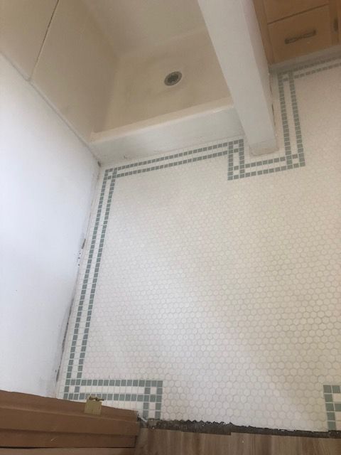 Small bathroom with white mosaic tile floor, beige walls, and a wooden vanity cabinet.