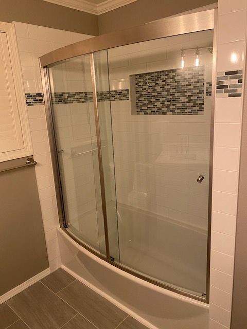 Curved glass shower enclosure with sliding doors, white tile walls, and gray floor in a bathroom