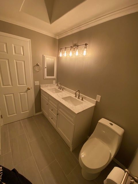 Modern bathroom with double vanity, large mirror, wall lights, and toilet in beige tones