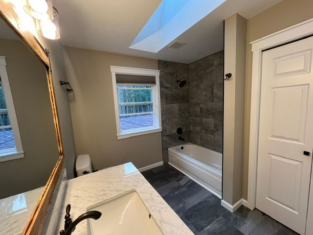 Modern bathroom with double vanity, freestanding tub, tiled shower, and skylight.