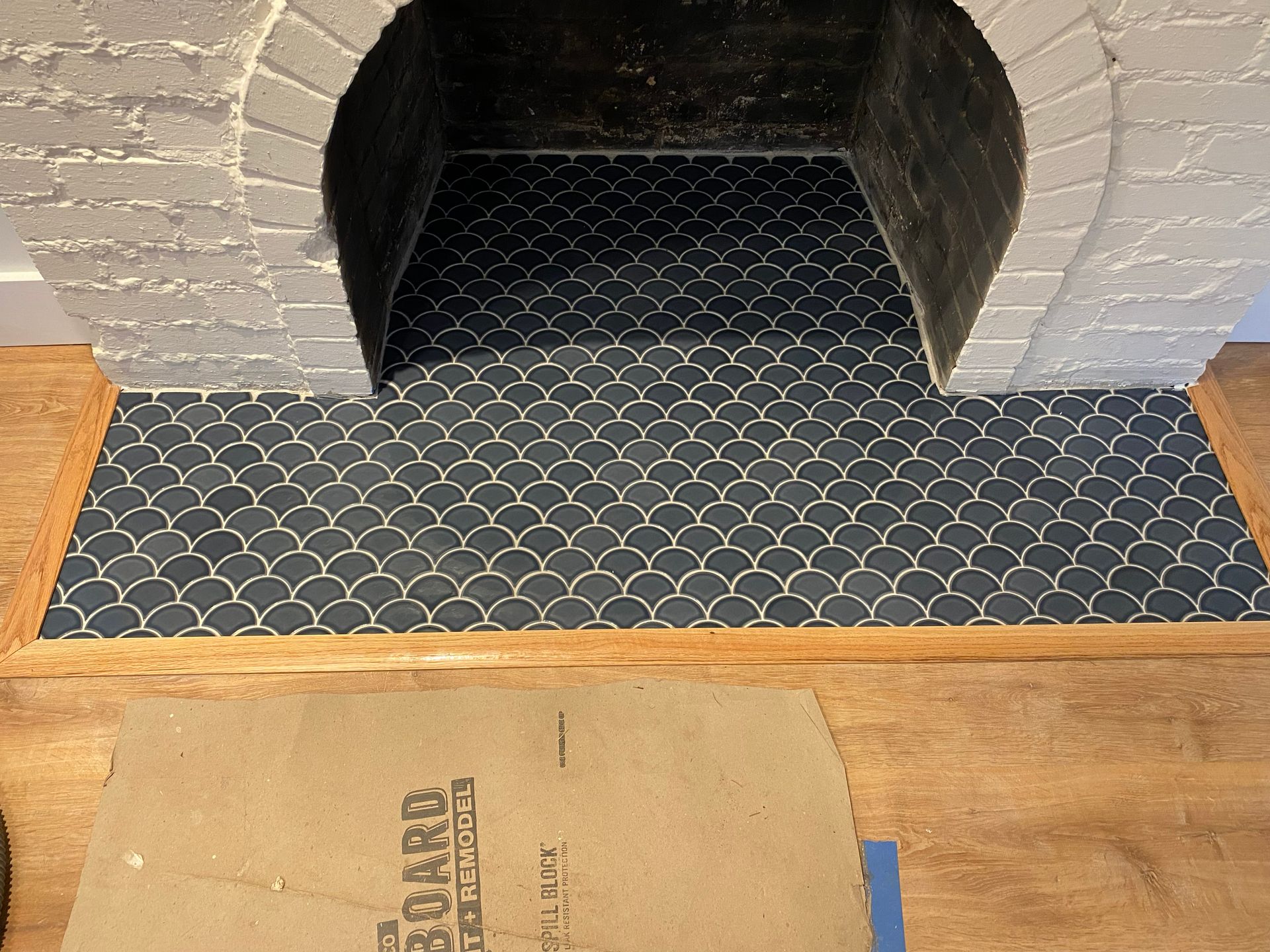 Blue patterned fireplace mat in front of a brick hearth with a tan rug in the foreground