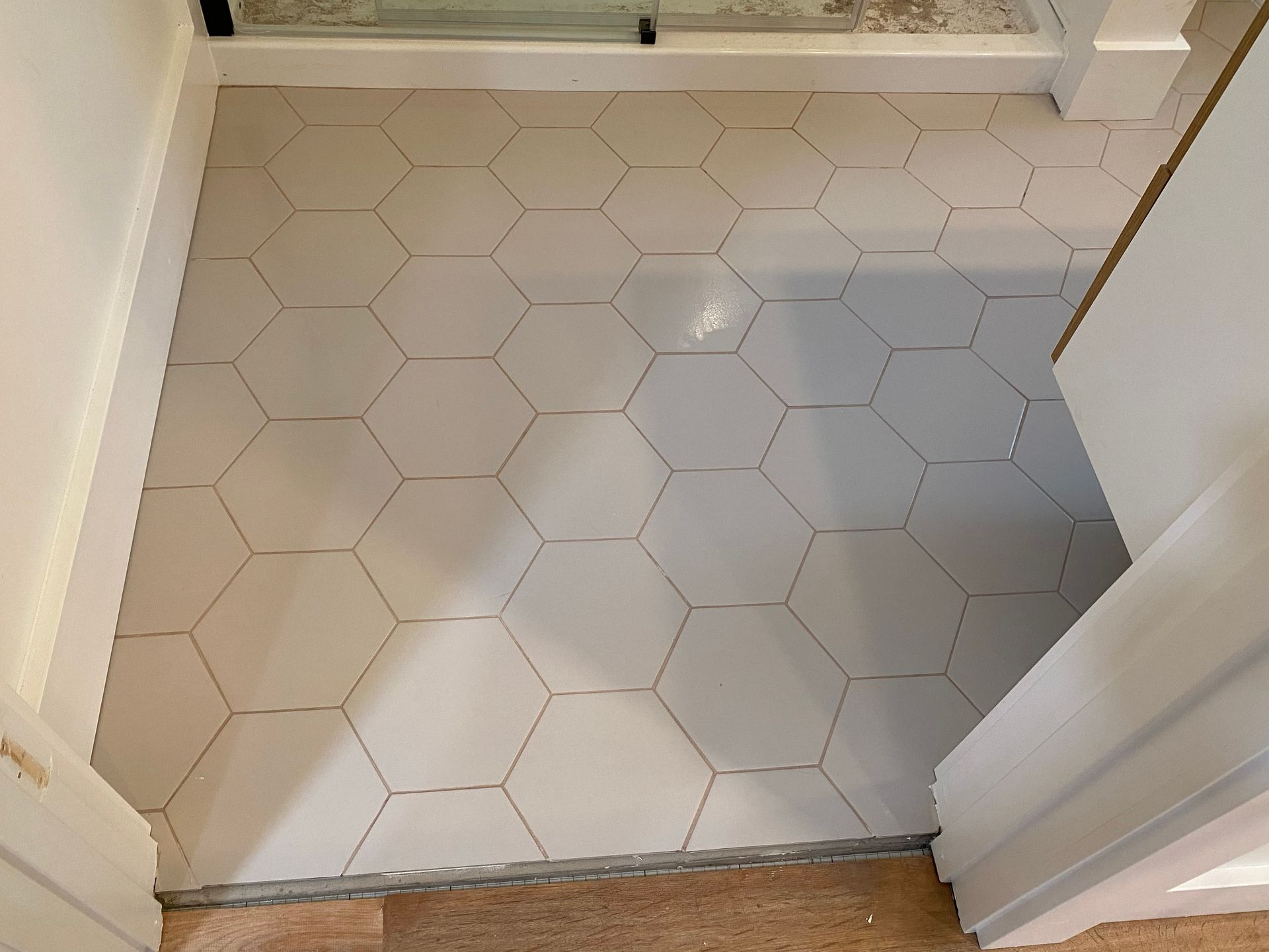 Small white hexagonal tile floor in a doorway or bathroom entrance with a metal threshold.