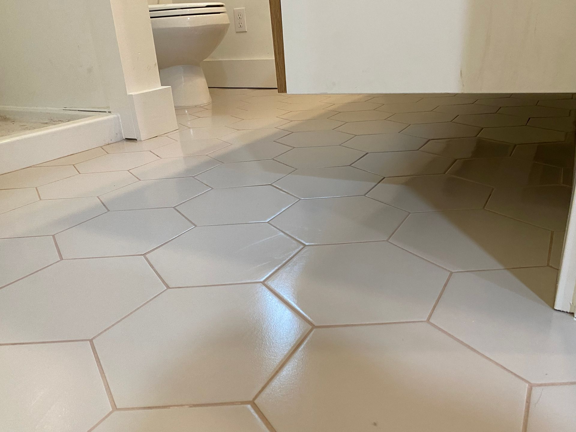 White hexagonal tile floor in a bathroom, with a toilet and door in the background.