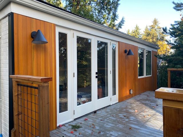 Modern tiny house exterior with white French doors, wood siding, and a paved patio