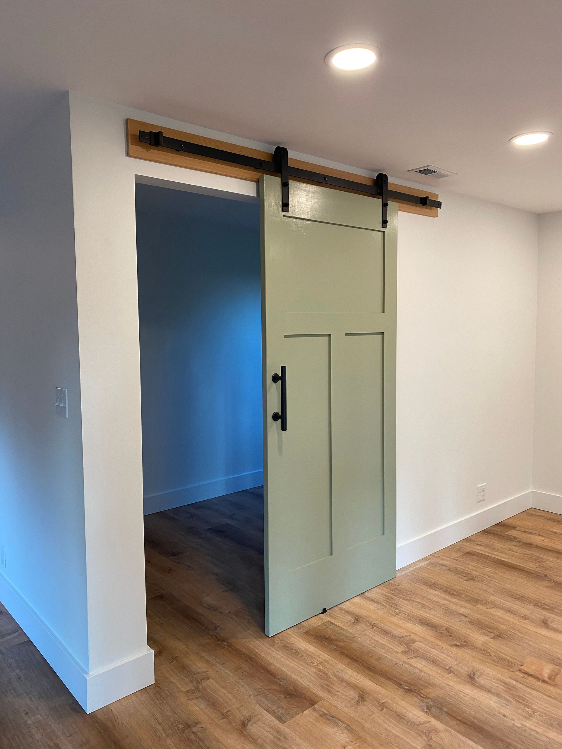 A pale green sliding barn door partly open in a white room with wood flooring.