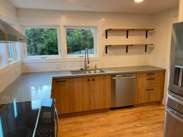 Modern kitchen with wood island, stainless appliances, white cabinets, and large windows overlooking greenery