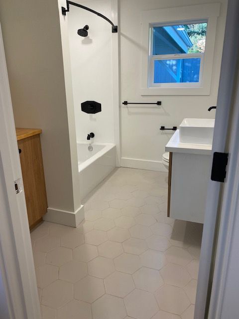 Bright bathroom with tub-shower, sink, white hex tile, and small window.