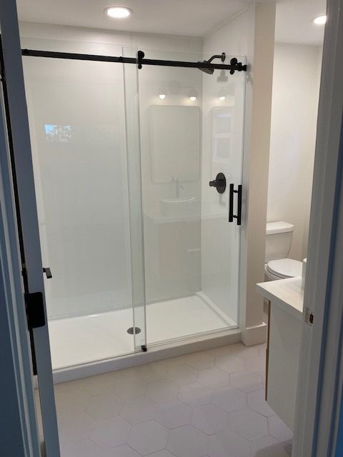 Modern bathroom with glass-enclosed shower, white tile floor, and vanity sink on the right