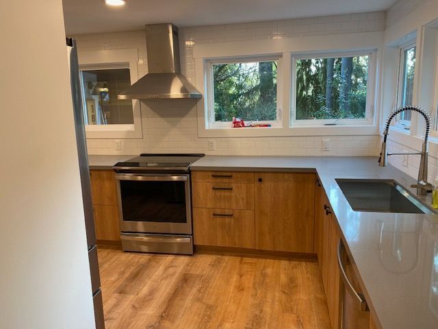 Modern kitchen with stainless steel stove, wooden cabinets, white countertops, and a large window.