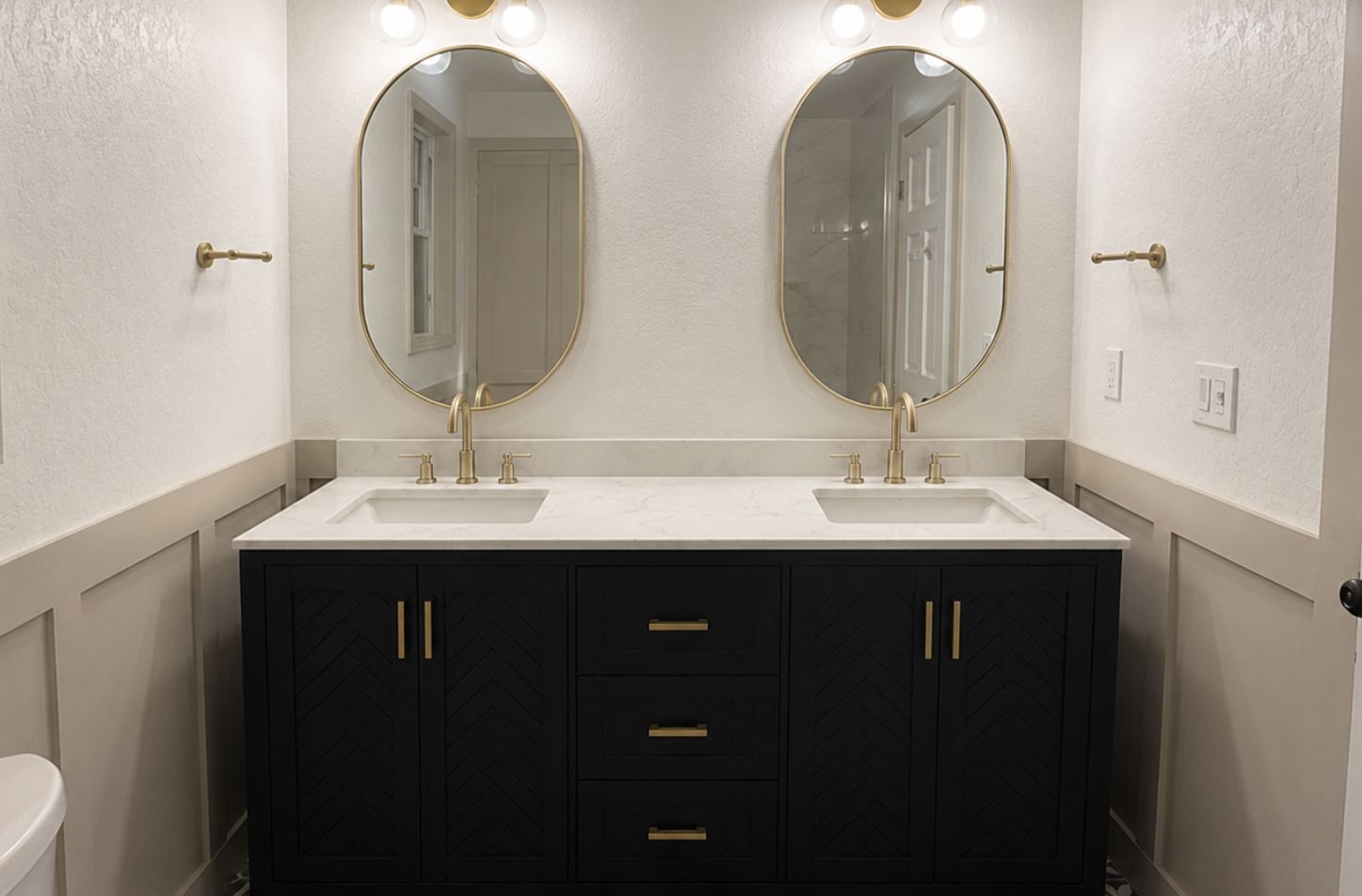 Modern bathroom vanity with two oval mirrors, gold fixtures, and a black cabinet with a white countertop