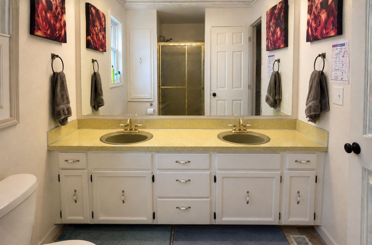 Bathroom vanity with double sinks, large mirror, and white cabinets with a yellow countertop.