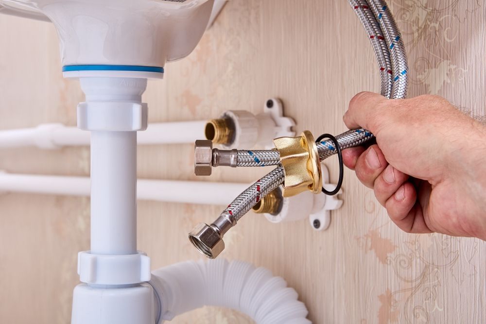 Hand installing a chrome faucet connector under a sink with a wrench