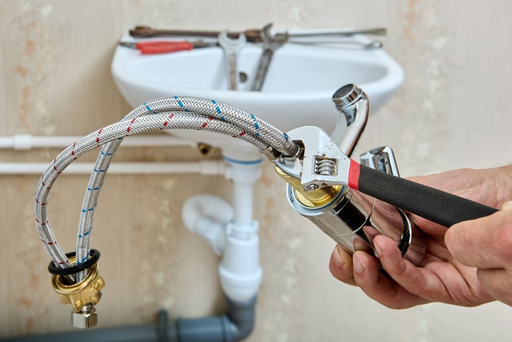 Hands using a wrench to tighten a braided water supply line under a sink.