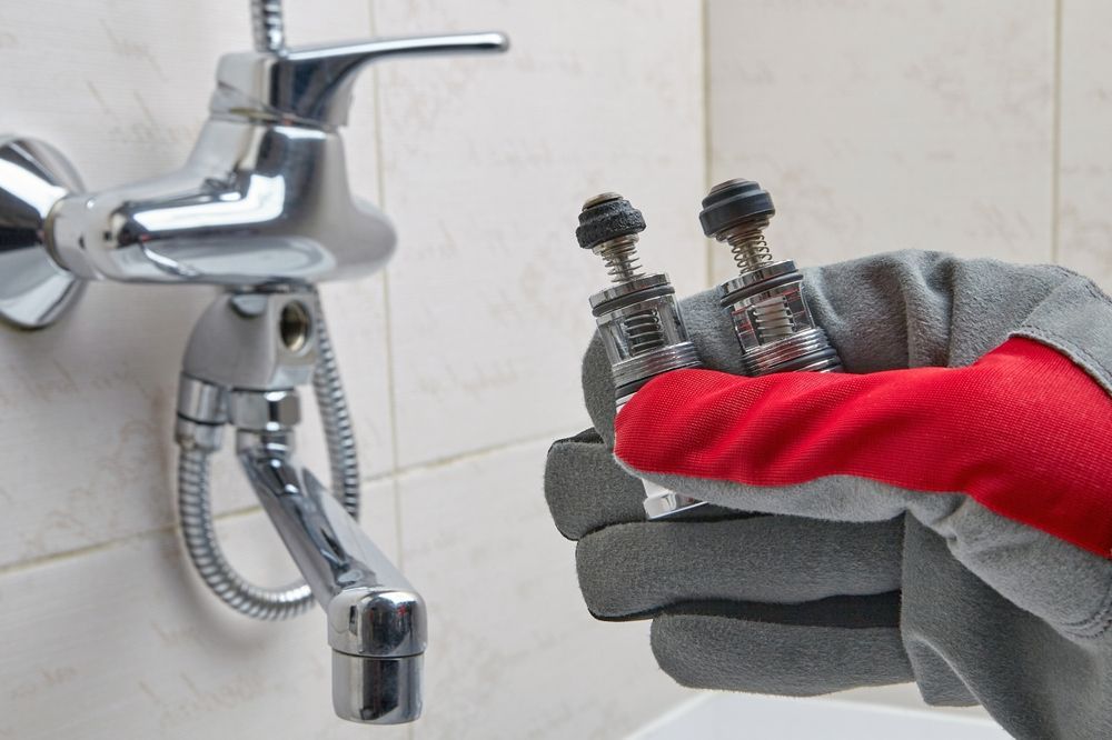 Gloved hand holding two metal faucet valves beside a chrome bathroom tap
