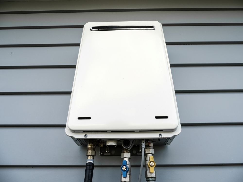 White wall-mounted boiler with pipes and valves against gray siding