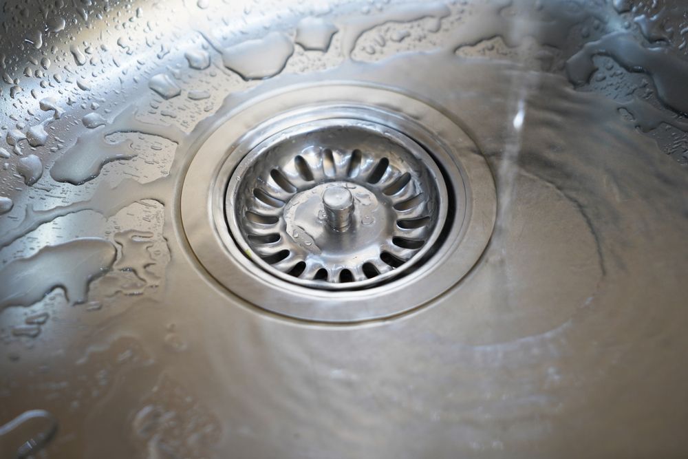 Close-up of a stainless steel kitchen sink drain with water and residue around it