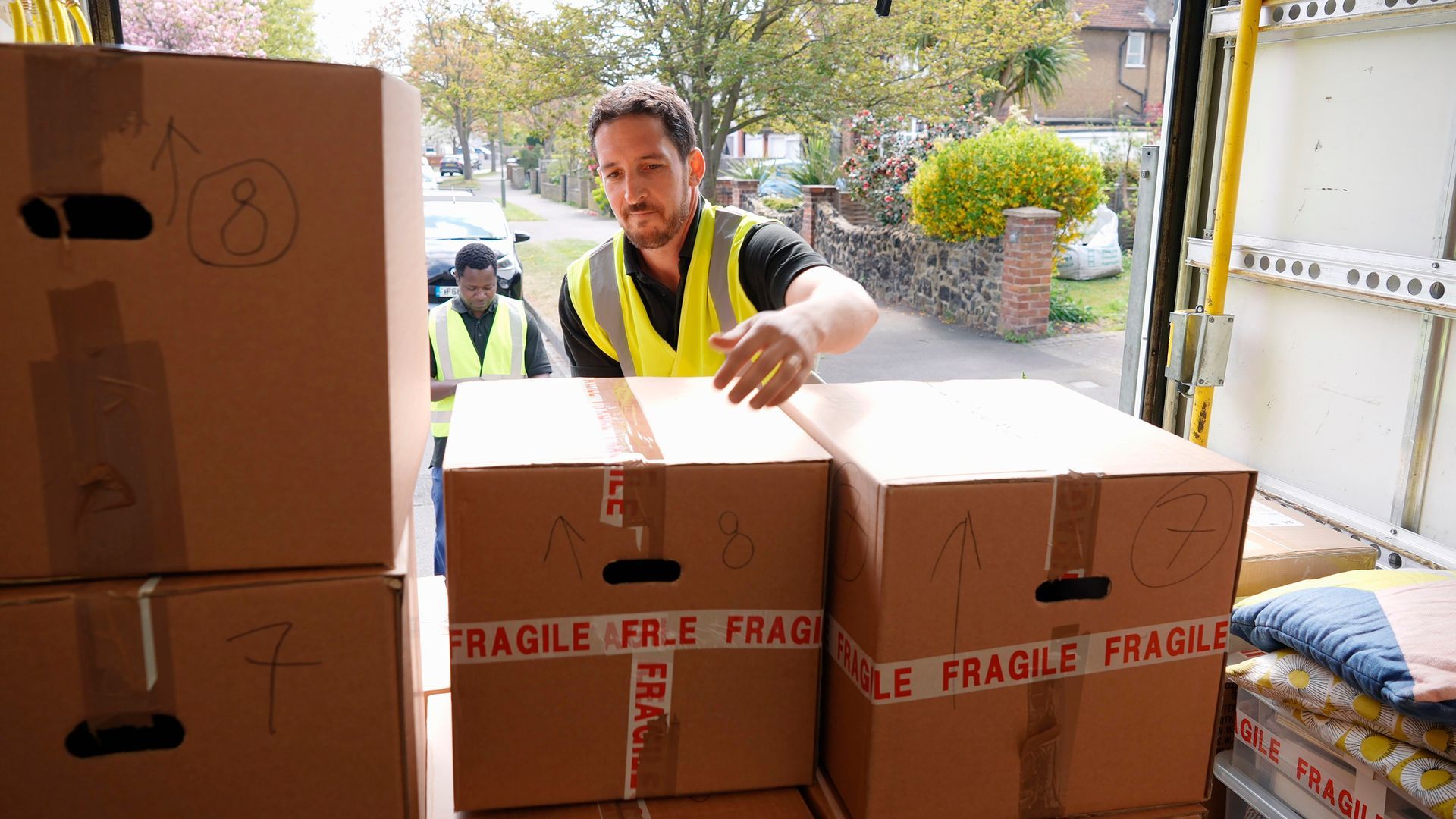 Delivery workers unloading cardboard boxes from a van on a residential street.