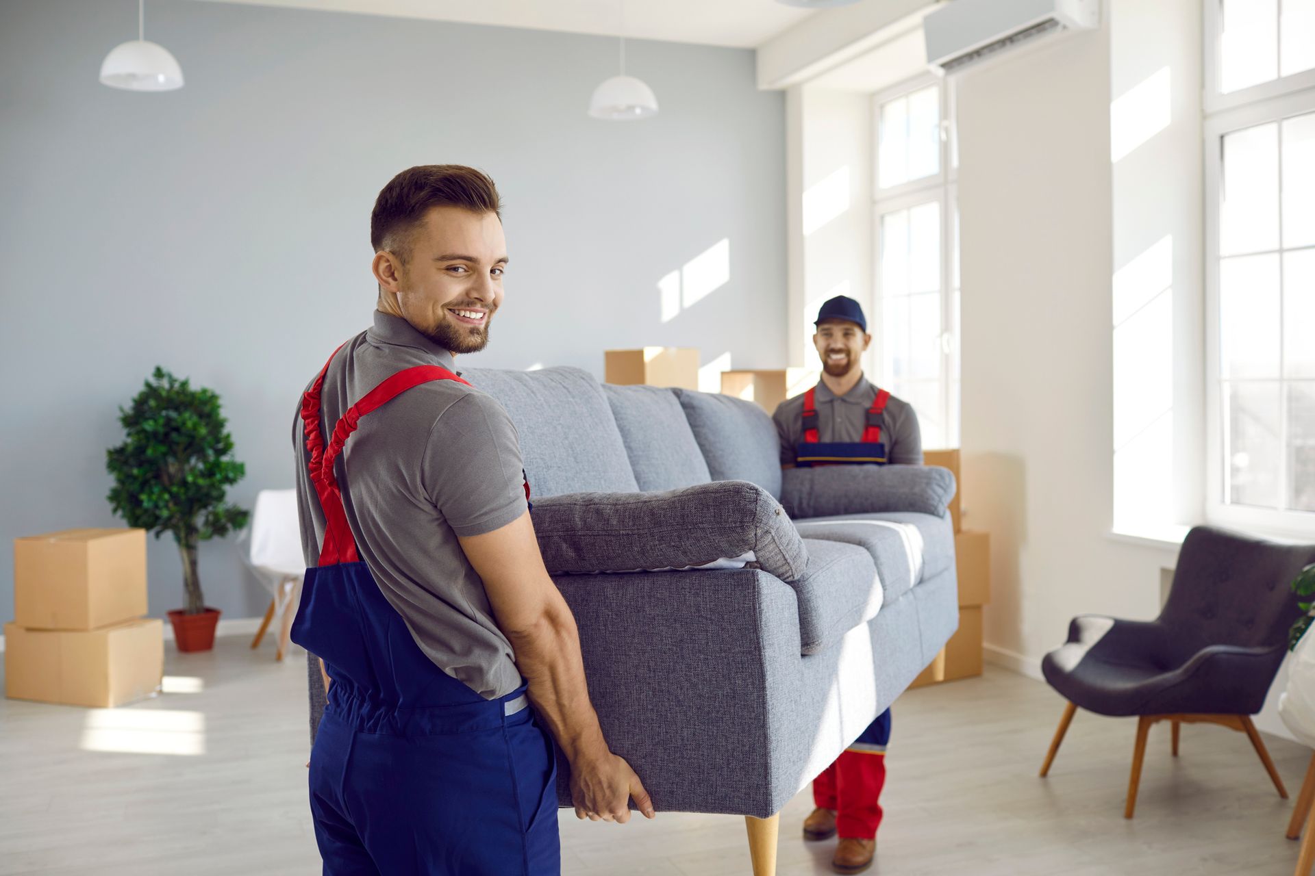 Two movers carrying a sofa in a light-filled room with boxes, smiling.
