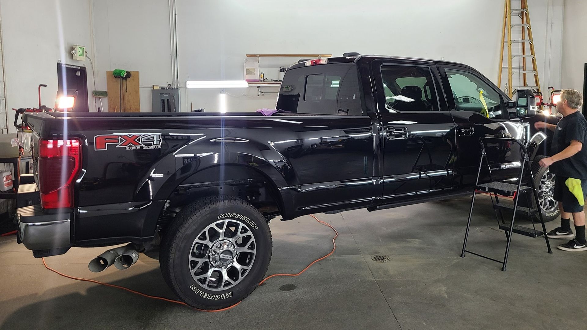 A man is working on a black truck in a garage.