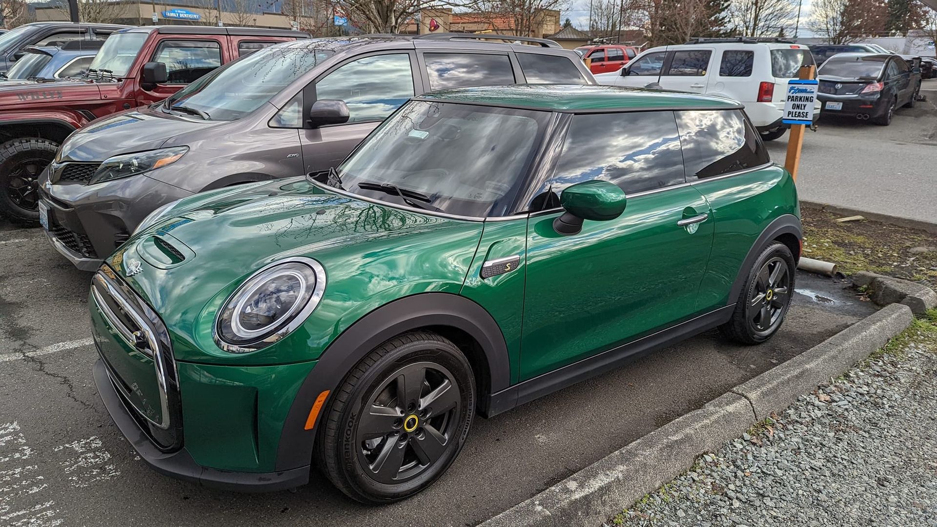 A green mini cooper is parked in a parking lot next to other cars.