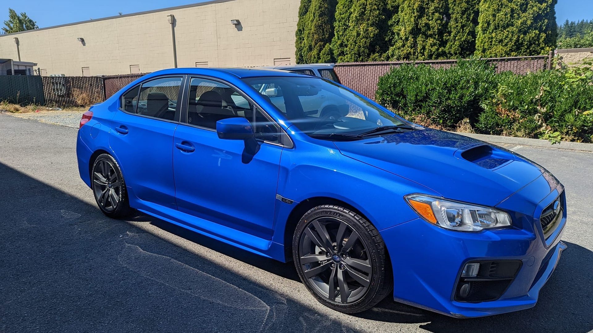 A blue subaru wrx sti is parked in a parking lot in front of a building.