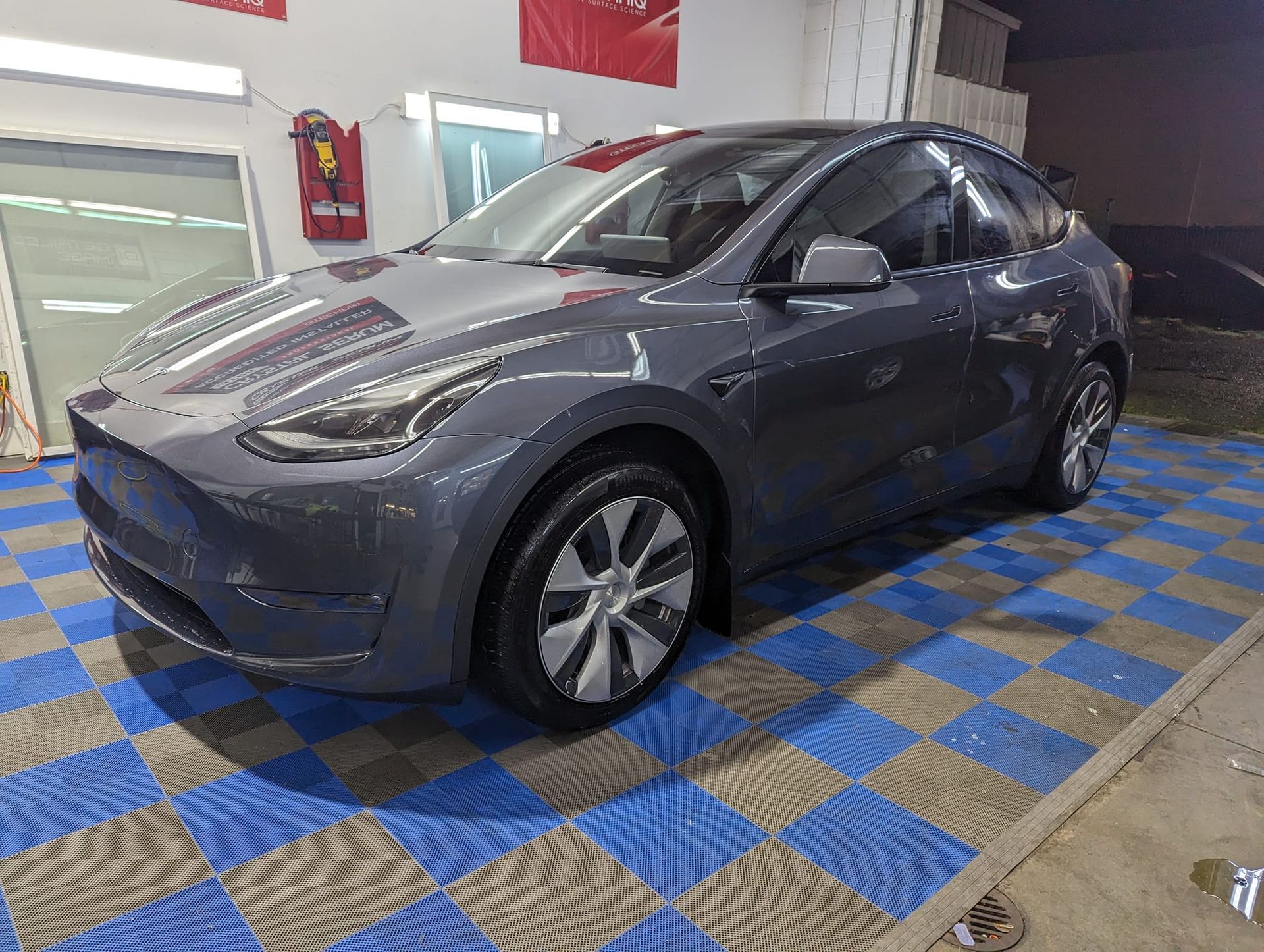 A tesla model y is parked on a checkered floor in a garage.