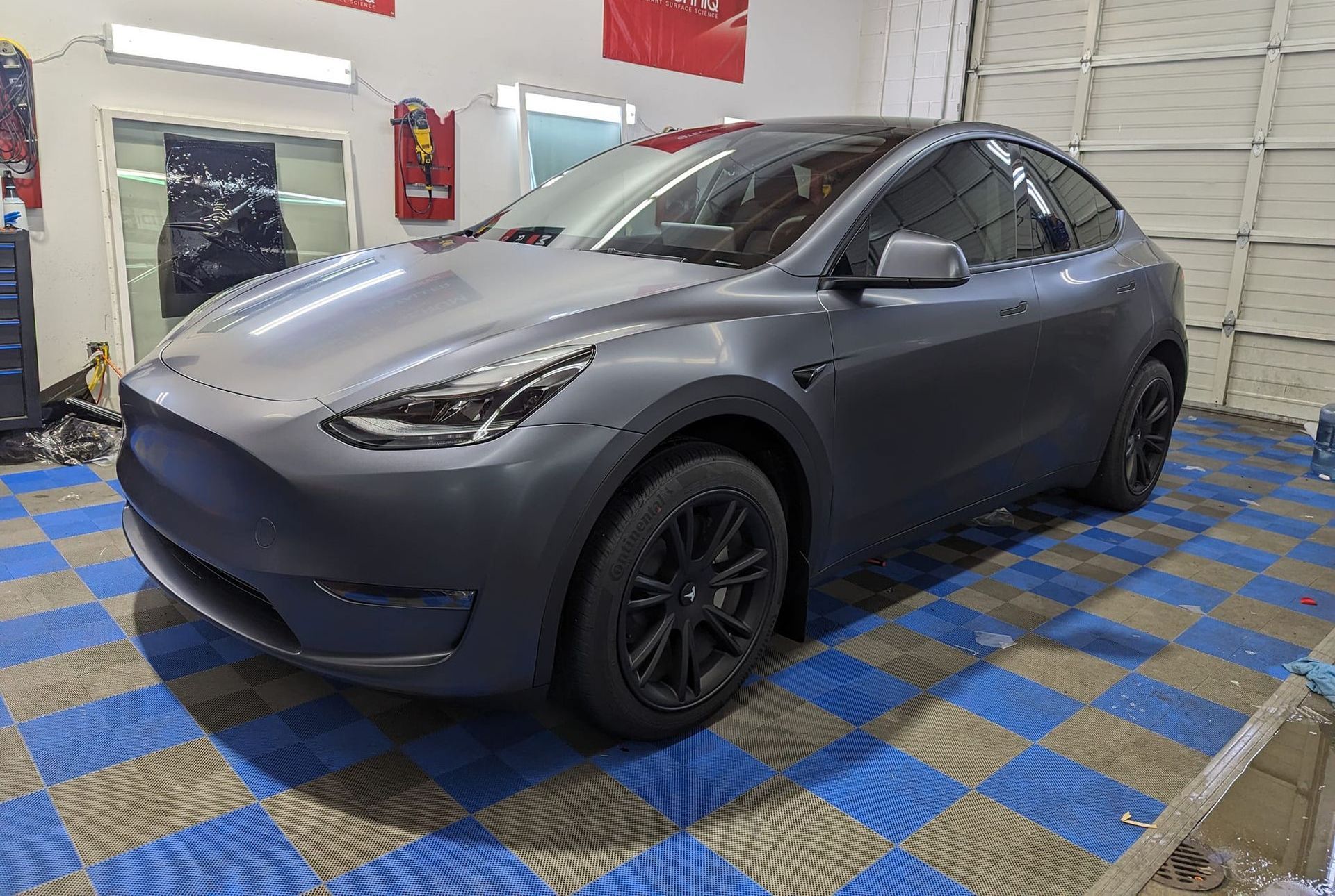 A tesla model y is sitting on a checkered floor in a garage.