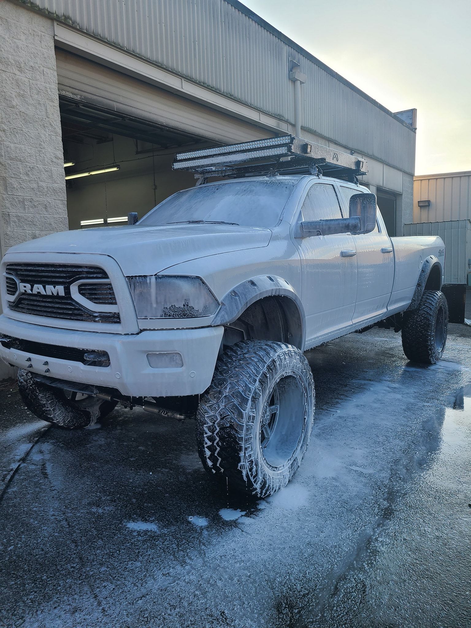 A white ram truck is covered in foam in front of a building.