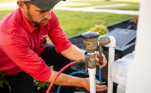 Man in red shirt adjusting outdoor sprinkler system, close up.