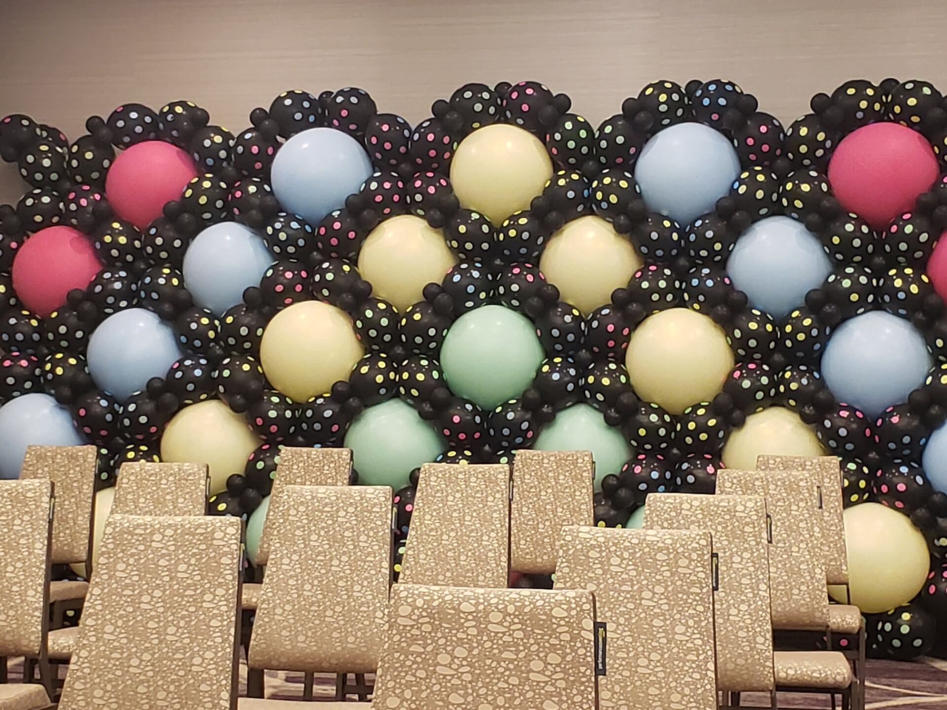 Custom balloon wall pattern with pink, pastel yellow, green and blue balloons, surrounded by black with polka dot balloons.