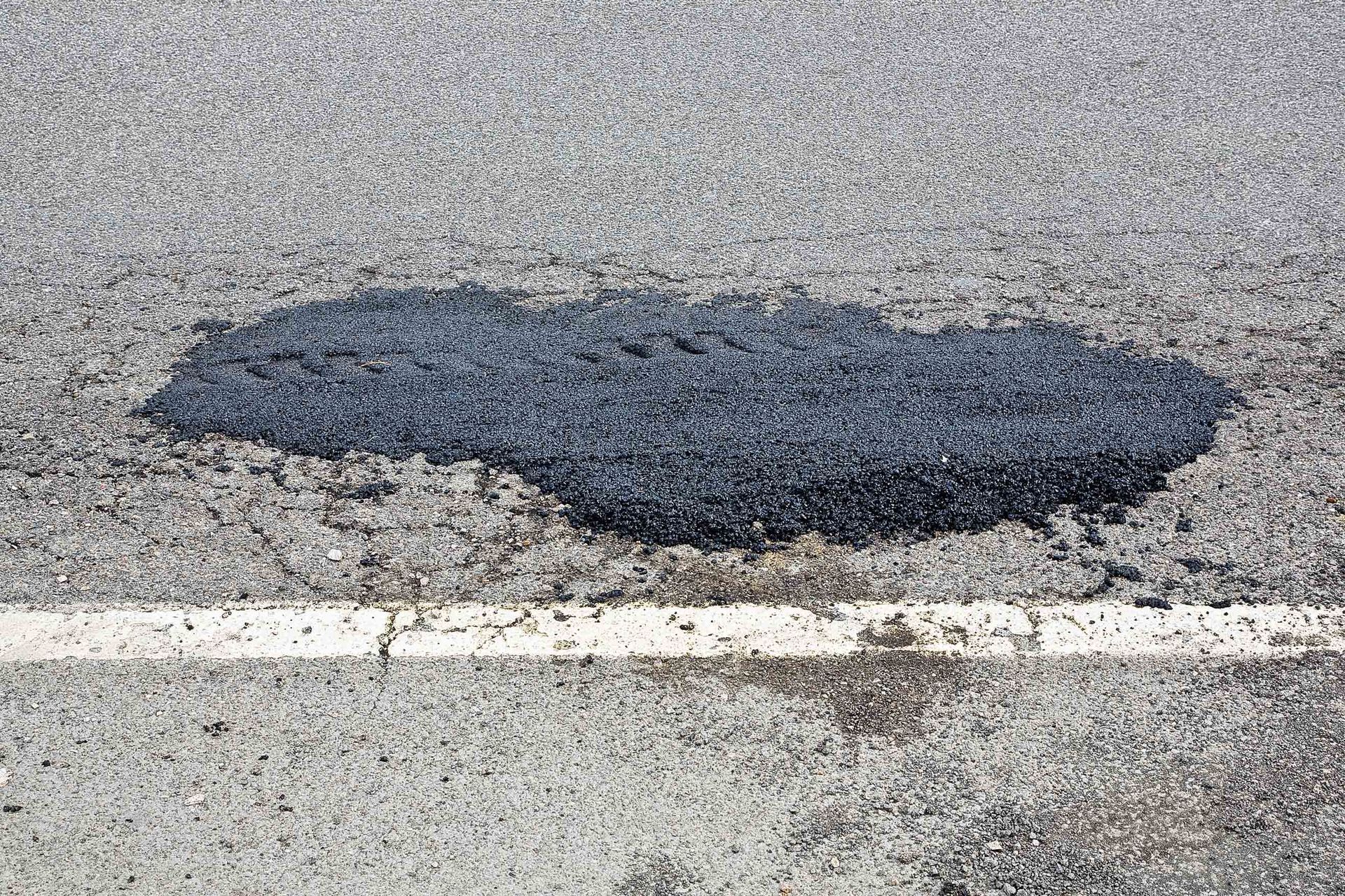Dark asphalt patch on a light gray road near a white lane line