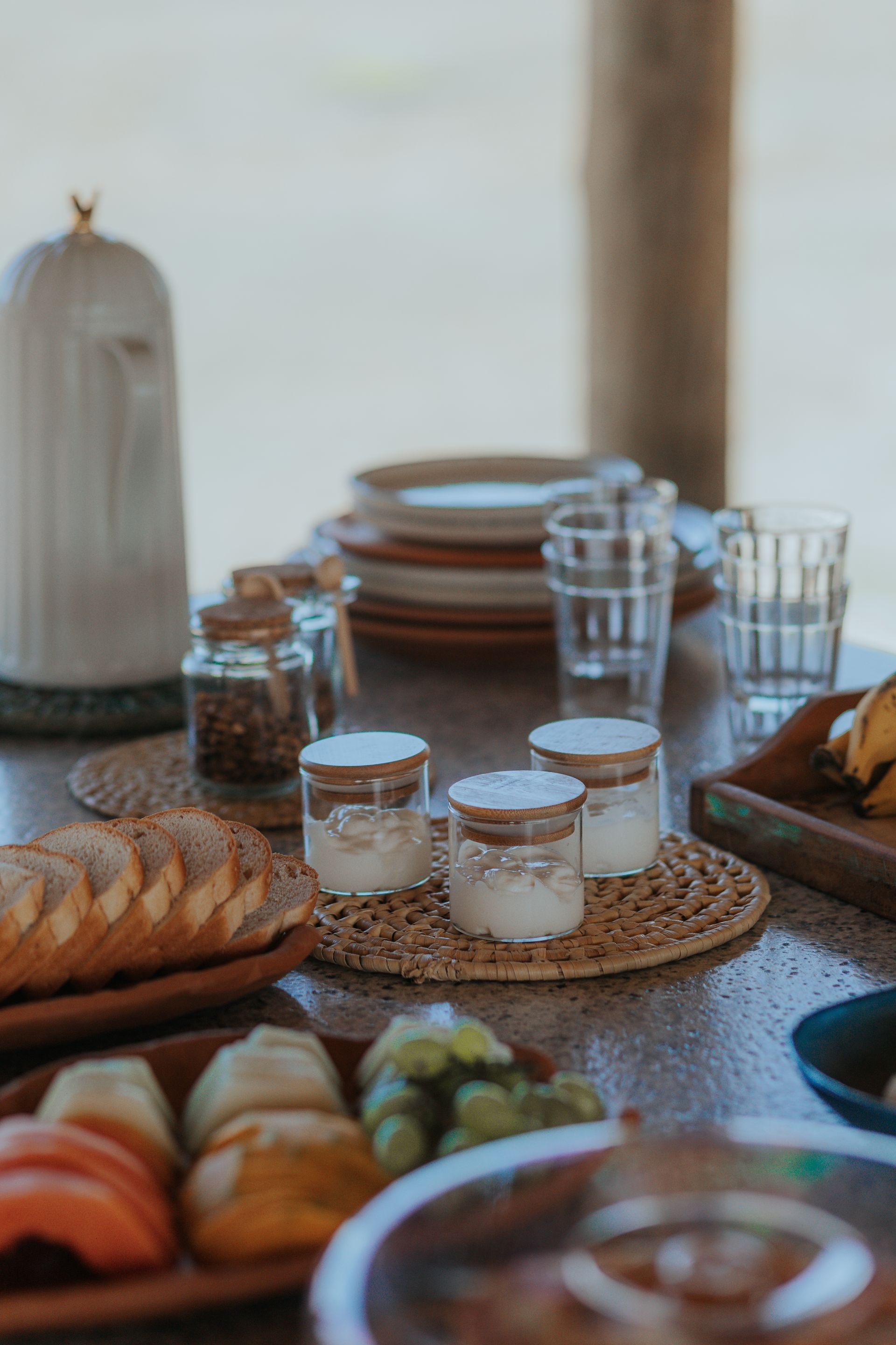 Mesa posta com sal, pão, frutas, pratos, copos e uma cúpula decorativa.