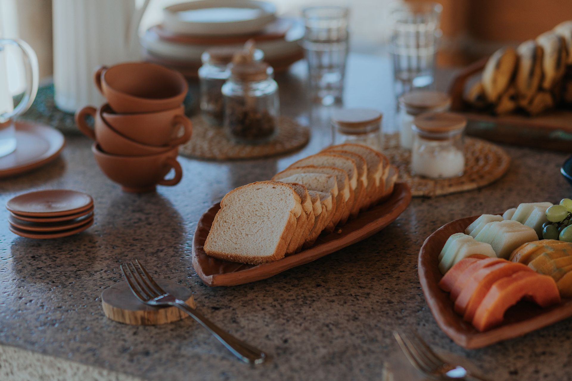 Mesa posta com pão, frutas e pratos de terracota.