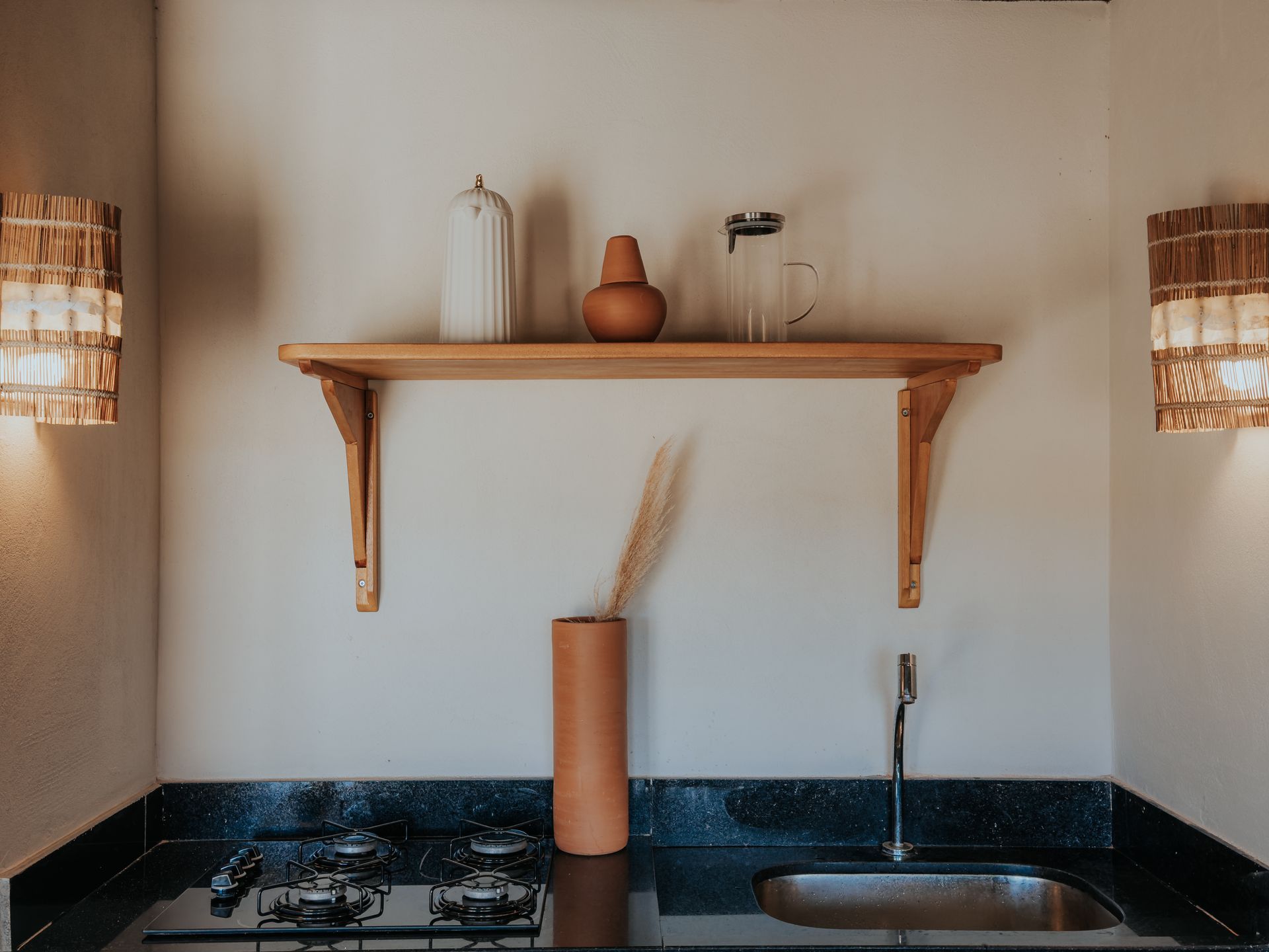 Cozinha com prateleira contendo peças de cerâmica e um vaso com juncos; bancada preta.