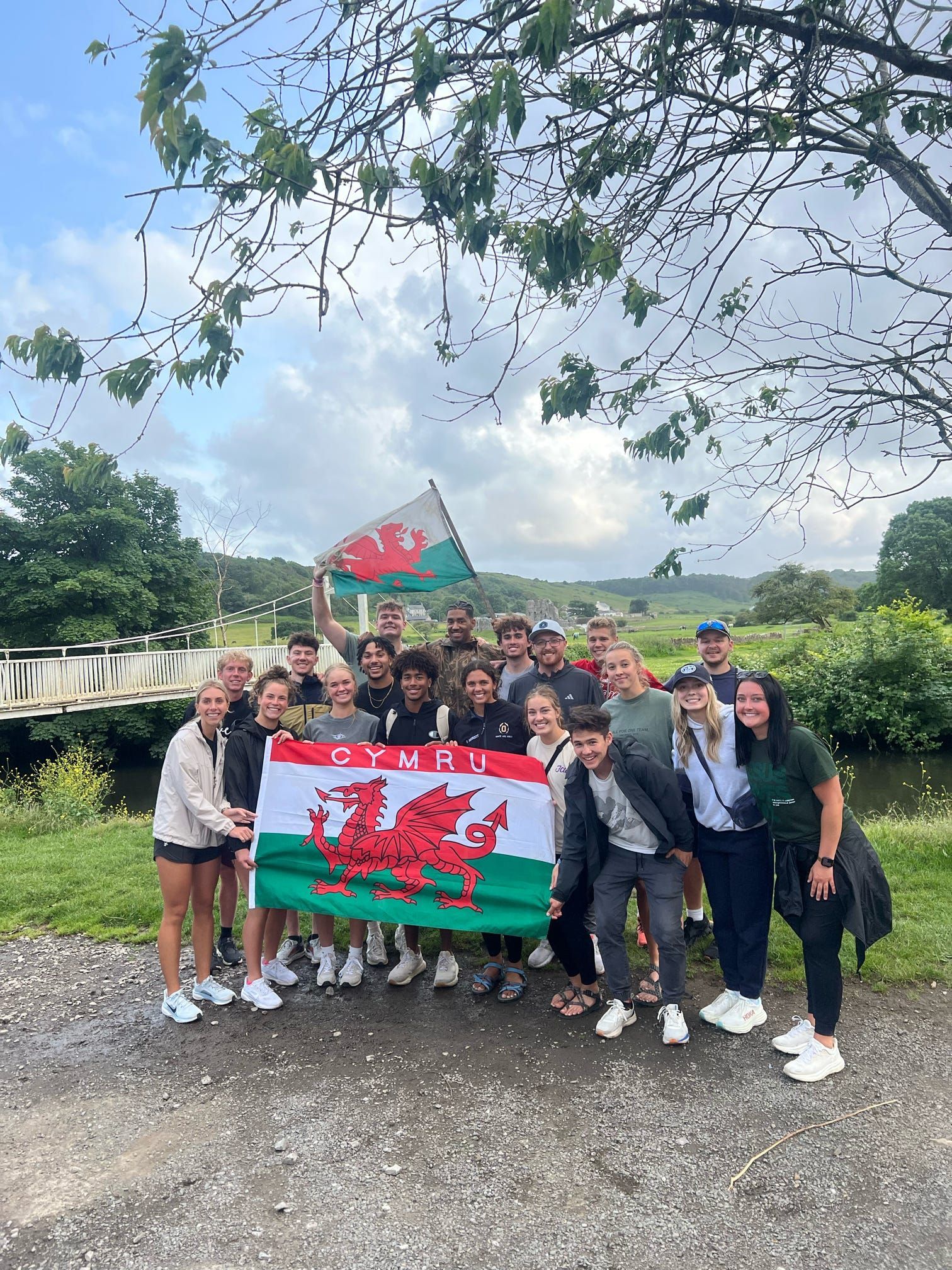 A group of people in sports clothes stand together waving a Wales Cymru flag.